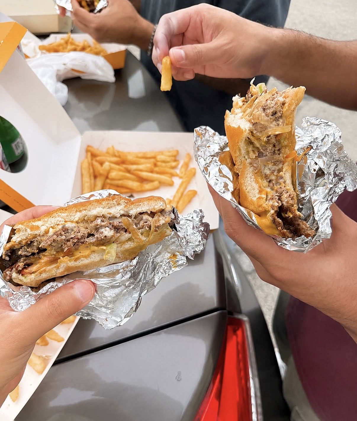 Two hands holding open smashburgers over boxes of golden fries